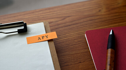 There is a notebook, a pen, and a clipboard with a sticky note stuck to it that says APY written on...