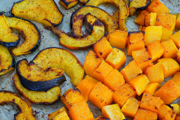 Roasted butternut squash cubes and acorn squash slices on parchment paper on a baking sheet