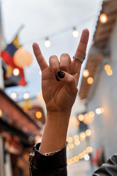 Man's hands with black painted nails, making a rock hand gesture, in the background a Colombian flag, rock al parque