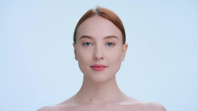 Young attractive ginger beauty model demonstrates results of applying eye cream, slides her fingers from under her eyes, looks at camera and smiles | beauty and skincare product ads concept