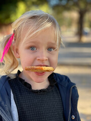 Close-up portrait of a lovely fair-haired girl looking funny with a biscuit in the teeth. She wants to have a snack after active games outdoors