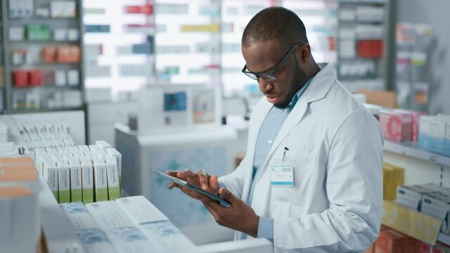 Pharmacy: Portrait of Professional Black Pharmacist Uses Digital Tablet Computer, Checks Inventory of Medicine, Drugs, Vitamins, Health Care Products on a Shelf