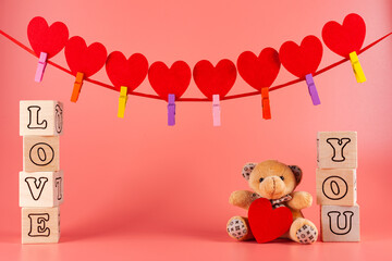 A teddy bear with a red heart. Wooden cubes with the inscription love you. A greeting card on a pink background. garland of red hearts on tape. Valentine's day background.