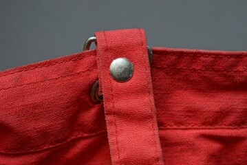 gray metal rivet and carabiner in a red cloth harness on an old bag