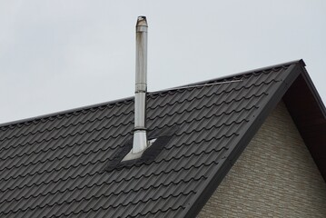 one long chimney from a white metal pipe on a brown tiled roof of a private house against a gray sky