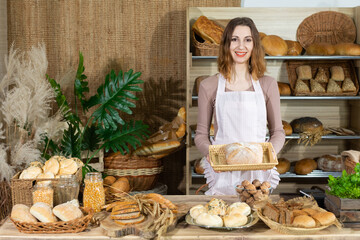 An attractive young saleswoman holds a loaf of bread in her hands. Family bakery shop with...