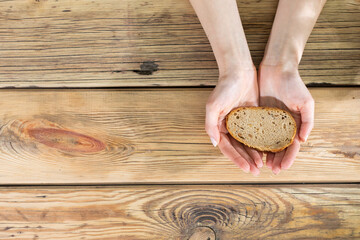 Girls' hands hold a slice of bread against the background of an old wooden table. A slice of bread for the needy.