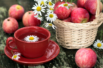 Still life with a cup of tea and red apples in a wicker basket on a wooden table in the garden.