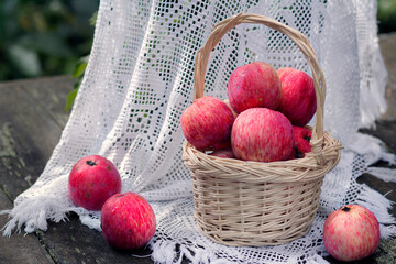 Still life with red apples in a wicker basket on a wooden table in the garden.