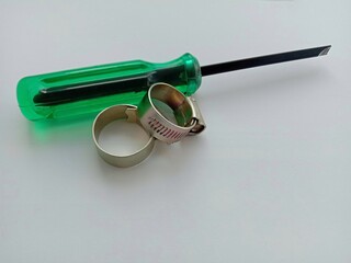 Metal hose clamps and screwdriver green handle isolated on white background closeup.