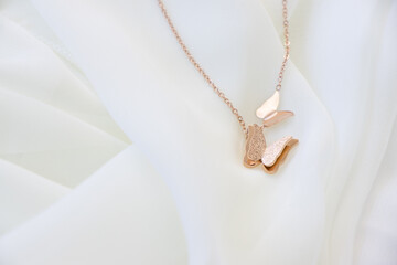 Closeup of a golden necklace with two butterflies pendant sitting on white silk