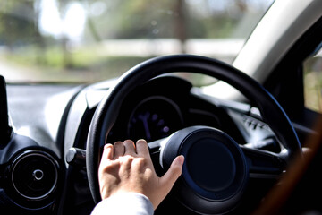 Close-up woman holding a car steering wheel, she is driving a car on a city street, car driving concept.