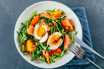 Healthy vegan salad of fresh tomato, arugula, salmon, egg and sesame on plate. Diet menu. Top view.