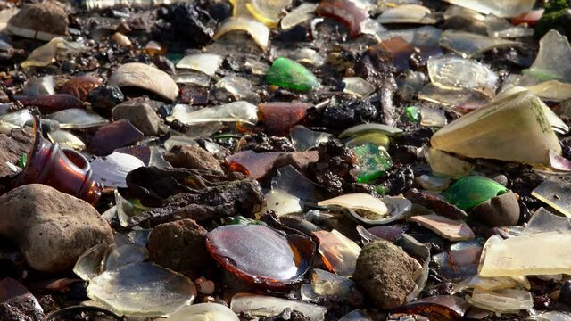 Littered beach in USA. Atlantic Ocean pollution, sandy beach covered by glass and garbage. Trash polluting Nature. Glass Bottle Beach in New York City