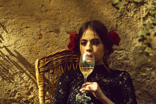 Spanish woman with wine. Adorable girl with stylish red lips, makeup on cute young face and roses in brunette hair holding wine glass on beige outdoor wall.