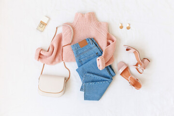 Blue jeans, pink knitted sweater, heeled sandals and small bag with chain strap on white...