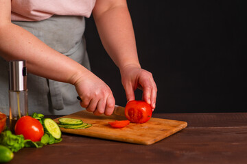 The chef cuts fresh vegetables on a wooden board. Cooking a burger.