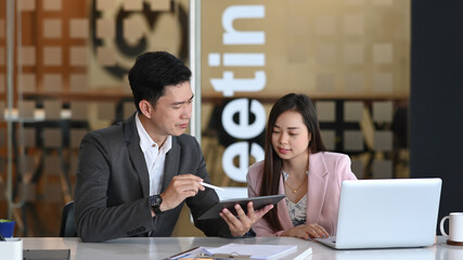 Photo of two businesspeople working with digital tablet and discussing about the project in the office.