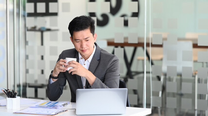 Businessman holding coffee cup and analyzing business online data  in laptop computer.