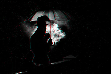 silhouette of a man in a hat under an umbrella Smoking a cigarette at night in the rain in the city