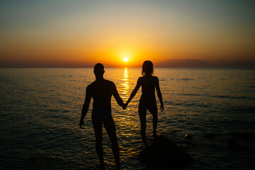 Romantic couple on the beach watching on sunset in twilight. Silhouette.