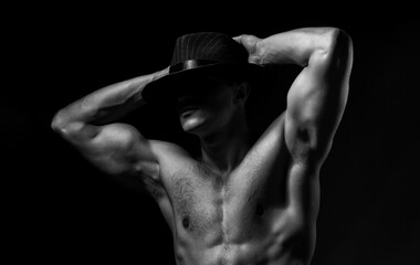 Fototapeta na wymiar Man in shadow. Young man with muscular body in hat with bare chest and torso posing in studio on black background.
