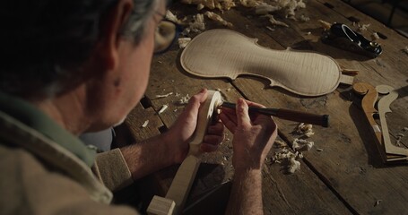 Cinematic shot of experienced master artisan luthier painstaking detail work on fine quality wood...