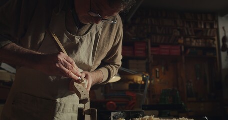 Cinematic shot of experienced master artisan luthier painstaking detail work on fine quality wood...