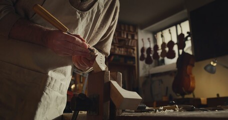 Cinematic shot of experienced master artisan luthier painstaking detail work on fine quality wood violin in creative workshop.Concept of spiritual instrument,handmade, art, orchestra, artisan,passion - obrazy, fototapety, plakaty