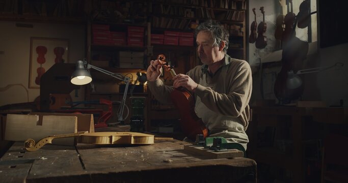 Cinematic shot of master artisan luthier working on creation of handmade fine quality wood violin in creative workshop. Concept of spiritual instrument, handmade, art, orchestra, artisan, music.