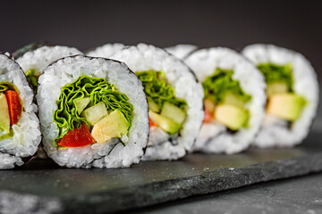 appetizing vegan sushi roll futomaki with pepper cucumber and avocado salad on a black stone plate