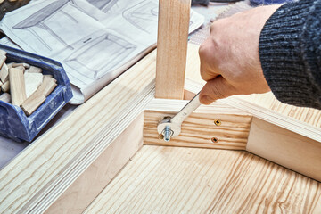 Skilled craftsman twists screw on joint gusset of table of plywood, veneer and solid light ash in...