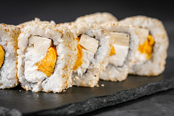 appetizing sushi roll california with tofu cheese and omelet on a black stone plate