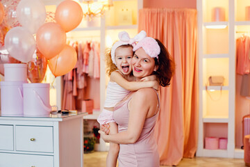 A beautiful young mother and her little daughter embrace, look at the camera and smile. Cuddle in the morning in the bedroom and dressing room with balloons. The concept of mother's day