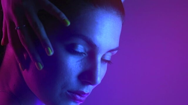 High Fashion model girl in colorful bright UV lights posing, portrait of beautiful woman with trendy make-up and manicure. Сolorful face make up. Over colourful purple background. Slow motion.