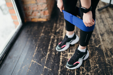 The girl pulls the elastic on her legs to do an exercise on the muscles of the legs