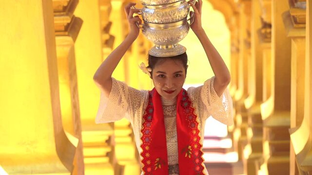 Young woman with traditional burmese holding bowl of rice on the head at beautiful golden pagoda in Myanmar.