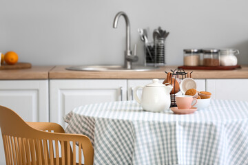 Teapot, cups and muffins on table in kitchen