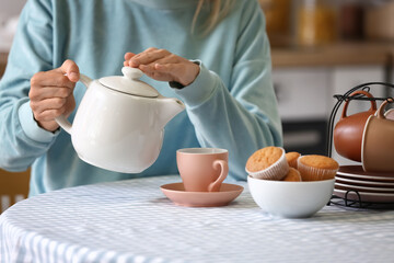 Woman pouring hot tea from teapot into cup at table
