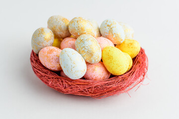 Mixed chocolate coated Easter eggs candies in a small red basket isolated on a white table, tasty sugary dessert for children.