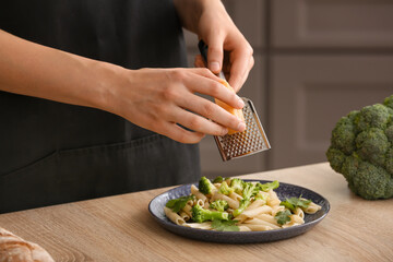 Woman grating cheese onto plate with tasty pasta, closeup