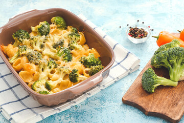Tasty pasta in baking dish and vegetables on color background
