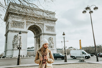 Young beautiful fashionable woman tourist in  white hat and scarf on background of  famous Arc de...