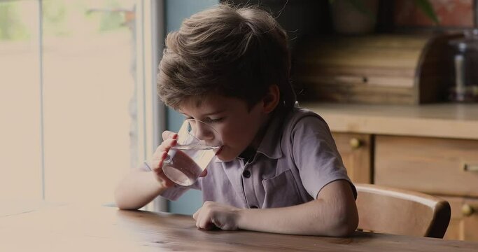 Head shot little adorable thirsty child boy drinking glass of clean pure mineral water, hydrating organism, refreshing alone in kitchen, healthy lifestyle, kids health care, good daily habit concept.
