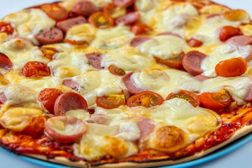 Fresh prepared tasty homemade pizza with tomatoes cherry, sausages and cheese close up