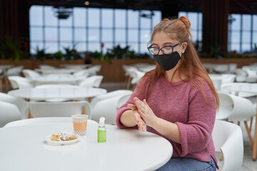 Young woman in protective mask applies sanitizer before lunch at fast food restaurant