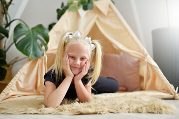Little girl with a smile in her room on the floor next to the wigwam tent © pridannikov