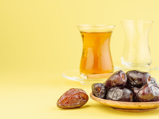 Dates with black tea on a yellow background. Traditional iftar food during Ramadan.