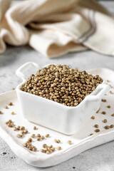 Hemp seeds. Peeled and whole dried hemp seeds in a white ceramic bowl on a light gray kitchen table. Hemp Seeds for Cooking	