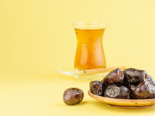 Dates with black tea on a yellow background. Traditional iftar food during Ramadan.